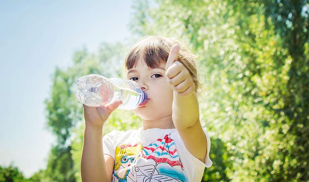 ילדה שותה מים מבקבוק בחוץ ומסמנת לייק עם האגודל