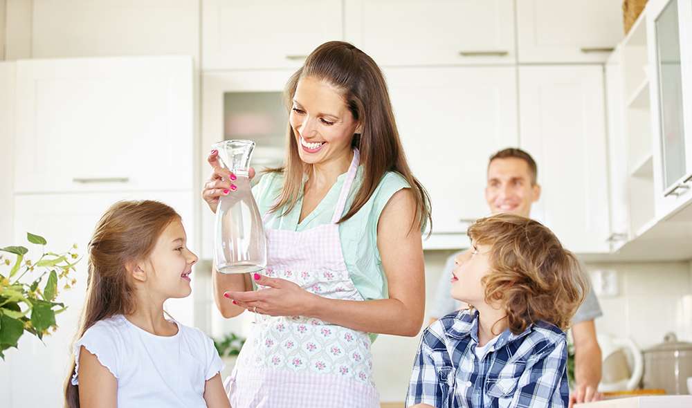 אמא מחזיקה קנקן מים ביד, יחד עם שני ילדיה ובעלה במטבח