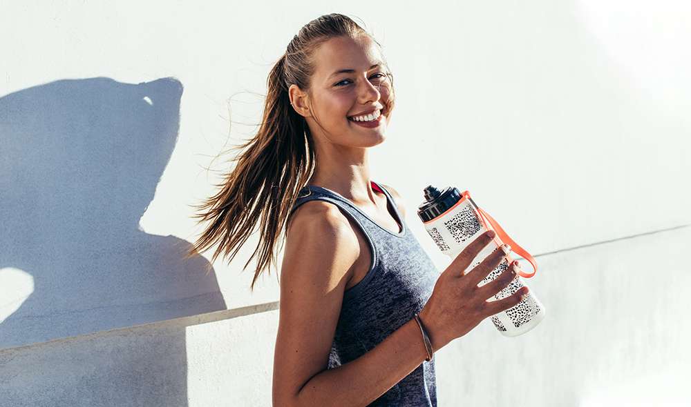 אישה בזמן אימון עומדת ליד קיר עם בקבוק מים ביד