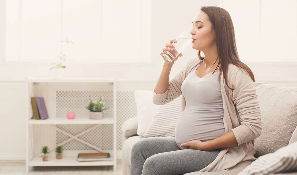 אישה בהריון יושבת ושותה מים
