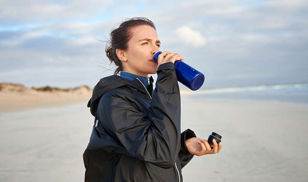 אישה שותה מים מבקבוק בחוף הים