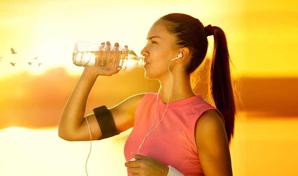 אישה בזמן אימון בחוץ שומעת מוזיקה באוזניות ושותה מים מבקבוק